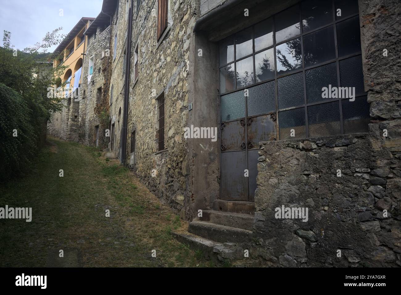 Schlampiger Kopfsteinpflasterweg zwischen einer Steinmauer und einem Steingebäude in den Bergen Stockfoto