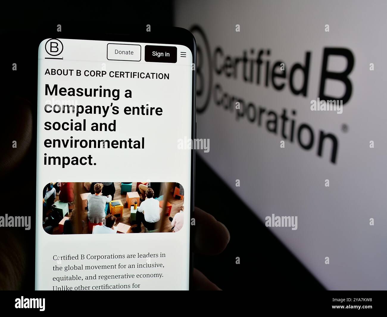 Person, die ein Mobiltelefon hält, mit Webseite der Zertifizierungsorganisation B Corporation (B Corp) auf dem Bildschirm mit Logo. Konzentrieren Sie sich auf die Mitte des Telefondisplays. Stockfoto