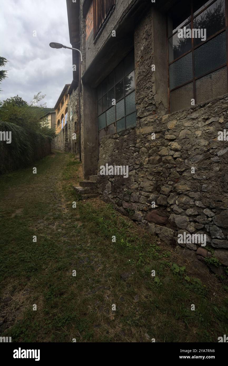 Schlampiger Kopfsteinpflasterweg zwischen einer Steinmauer und einem Steingebäude in den Bergen Stockfoto