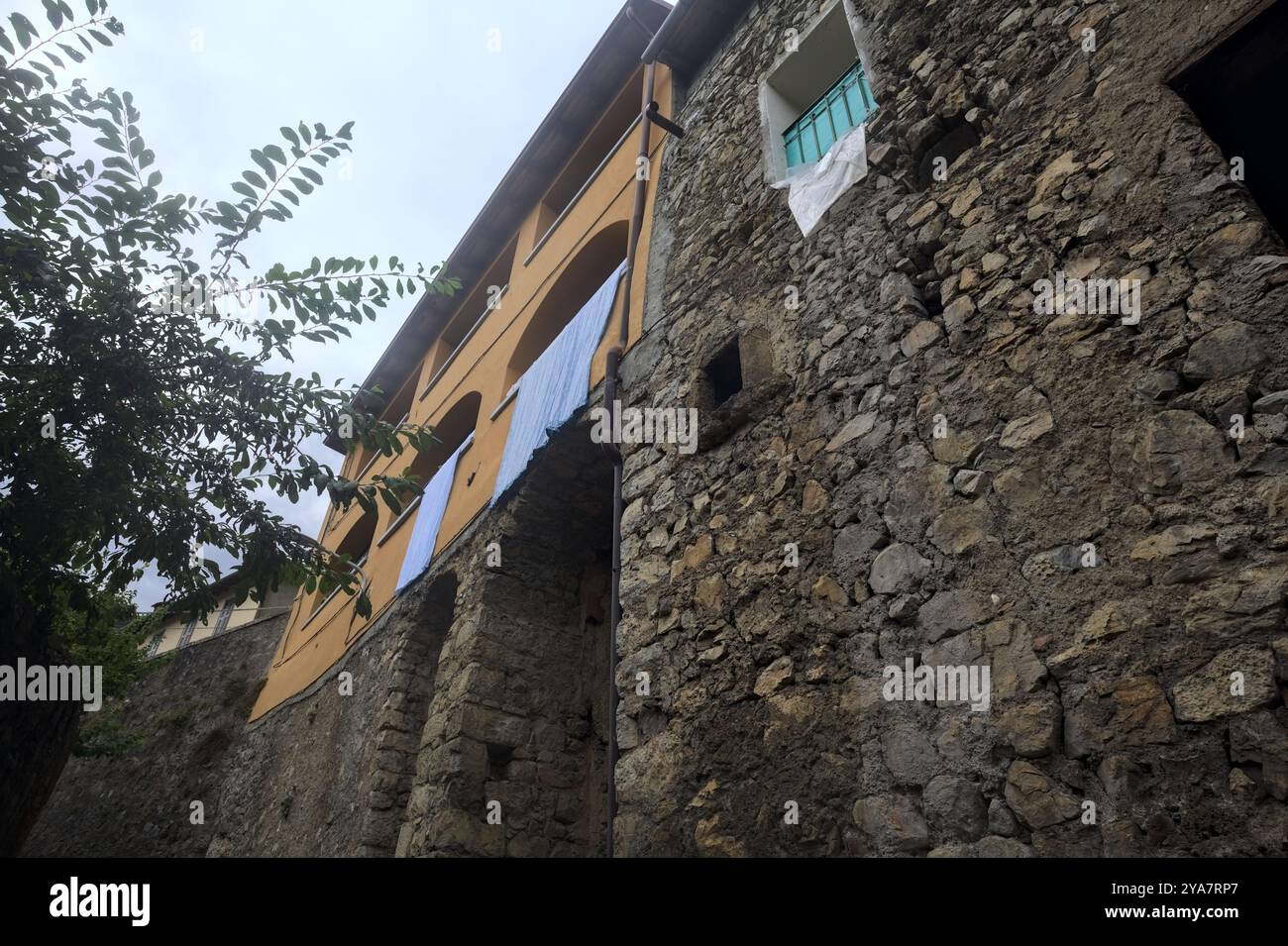 Schlampiger Kopfsteinpflasterweg zwischen einer Steinmauer und einem Steingebäude in den Bergen Stockfoto