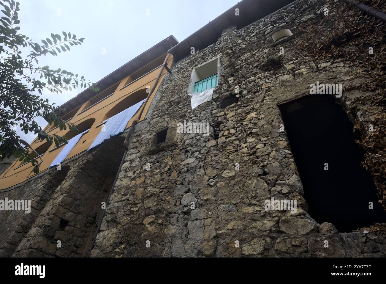 Schlampiger Kopfsteinpflasterweg zwischen einer Steinmauer und einem Steingebäude in den Bergen Stockfoto