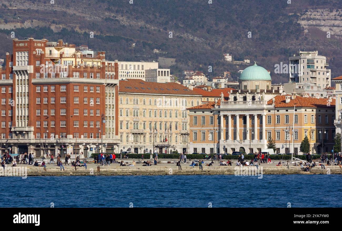 TRIEST, Italien - 9. März 2014: Skyline der Triester Küste mit ihren eleganten historischen Gebäuden und Menschen, die den sonnigen Winternachmittag genießen Stockfoto