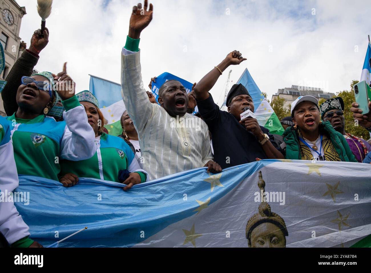 London, Großbritannien. Oktober 2024. Mitglieder der Yoruba-Diaspora stehen während der Kundgebung mit den Händen in der Luft hinter einer Flagge. Mitglieder der Yoruba-Diaspora hielten in Zentral-London eine Demonstration ab, in der sie einen unabhängigen freien Staat von Nigeria forderten. Quelle: SOPA Images Limited/Alamy Live News Stockfoto