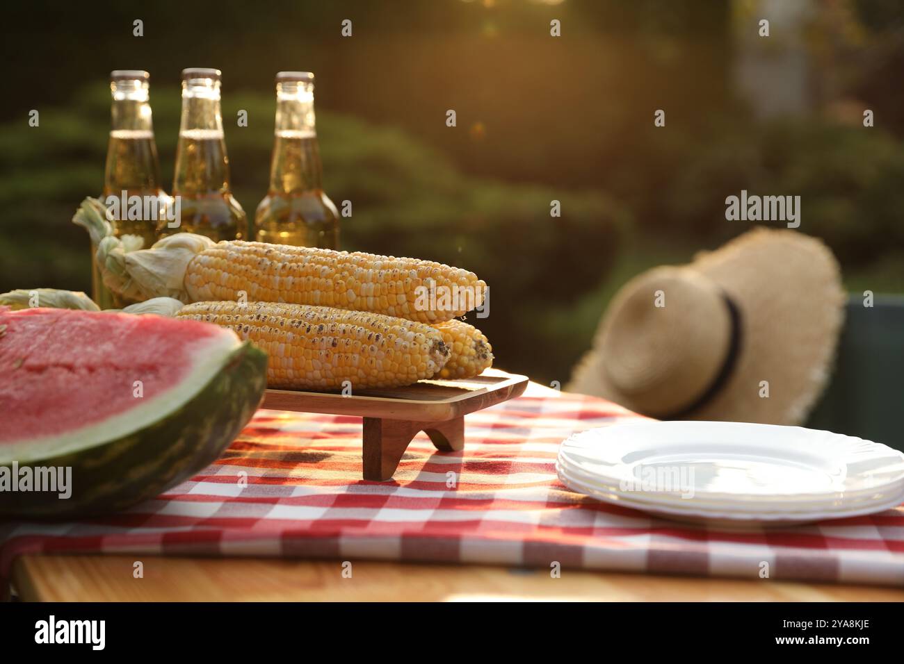 Frische Wassermelone, Mais, Teller und Getränkeflaschen auf dem Tisch im Garten Stockfoto