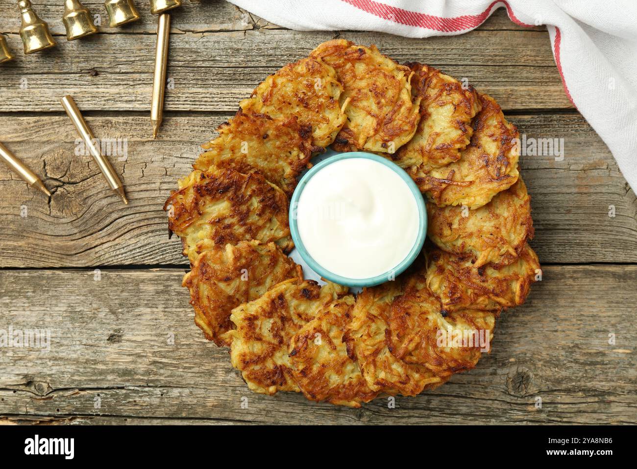 Leckere Kartoffelpfannkuchen, Sauerrahm, Menora und Kerzen auf Holztisch, flach gelegen. Hanukkah festliches Essen Stockfoto