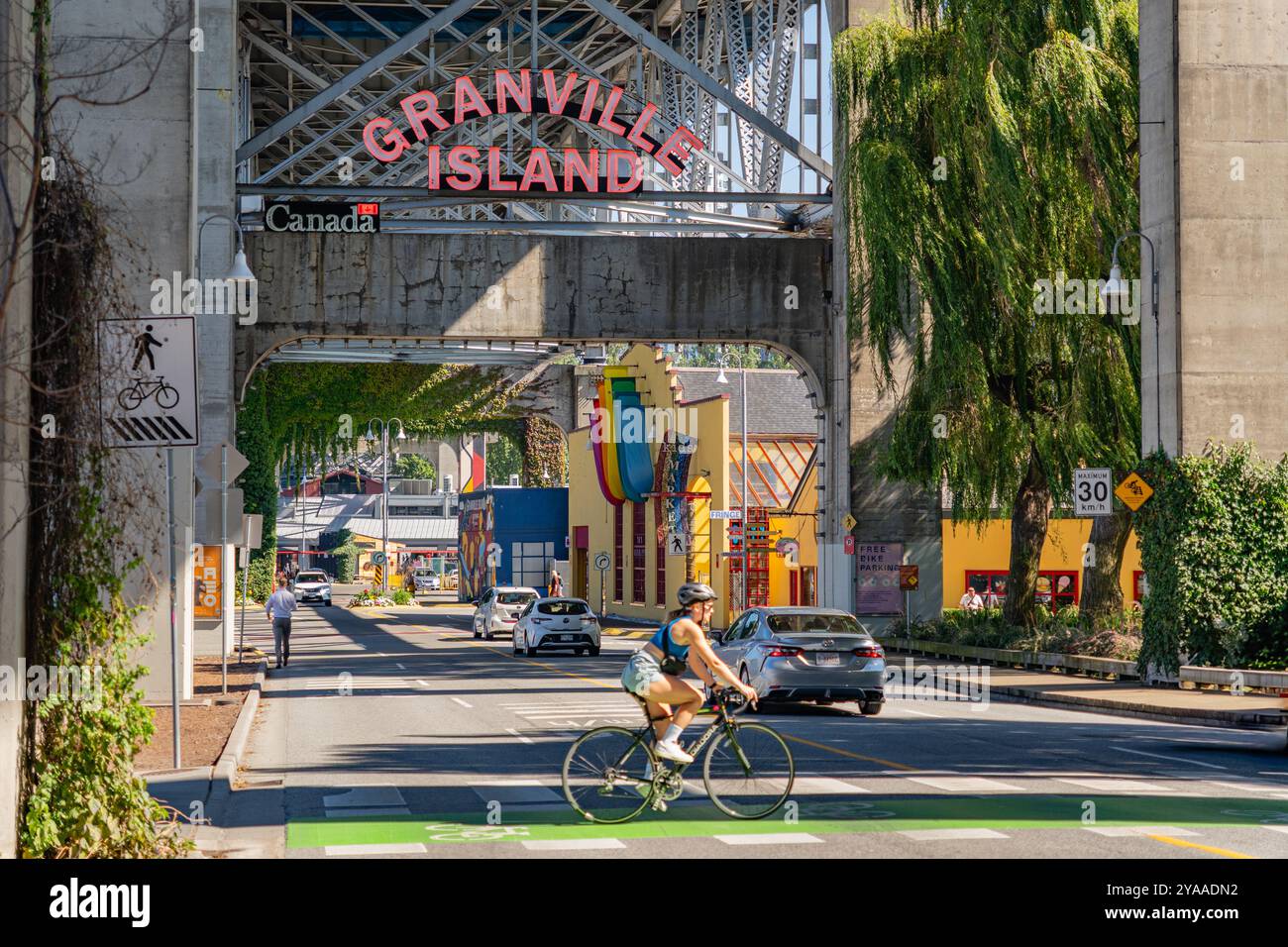 Vancouver, BC, Kanada, 4. September 2024: Granville Island Schild, ein öffentlicher Markt und Touristenattraktion mit Radfahrern im Vordergrund. Stockfoto