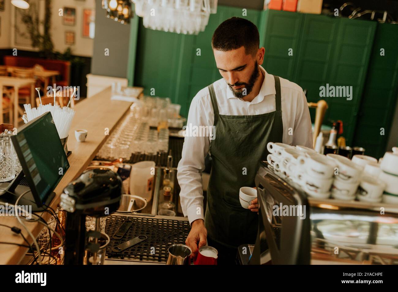 In einem warmen und einladenden Café gießt ein engagierter Barista fachmännisch Milch in eine Kaffeetasse und sorgt so für ein angenehmes Erlebnis für Gäste. Stockfoto