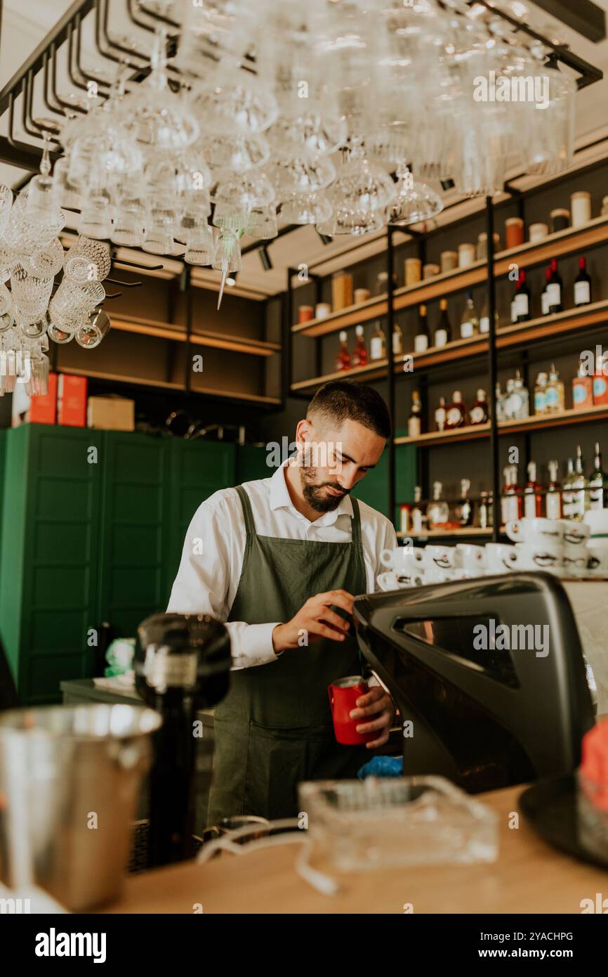 In einem schicken Café konzentriert sich ein erfahrener Barista auf die Herstellung köstlicher Getränke, umgeben von ordentlich angeordneten Gläsern und lebendiger Einrichtung, die eine warme Atmosphäre schaffen Stockfoto