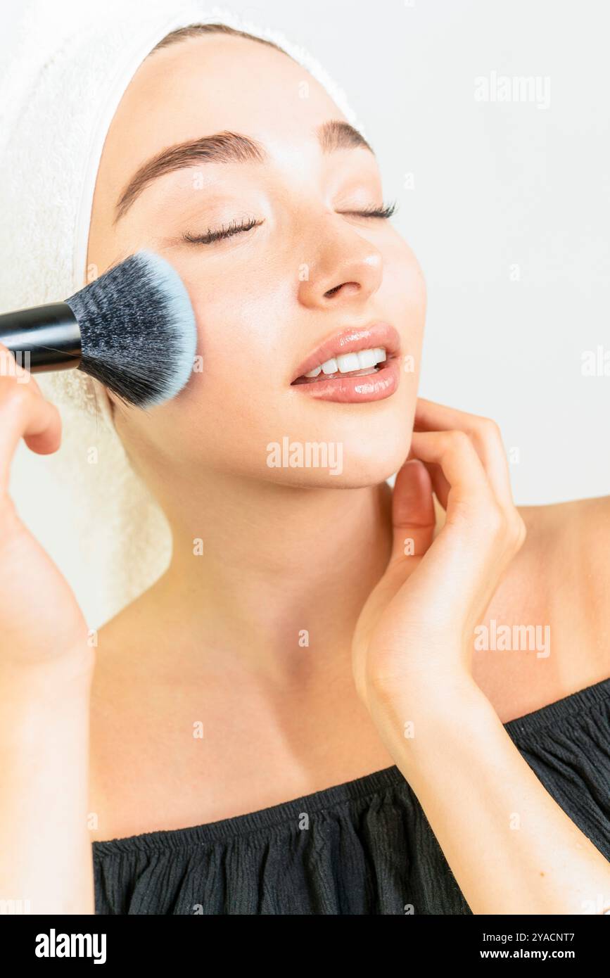 Eine Frau schminkt sich mit einem Pinsel. Sie lächelt und ist gut gelaunt Stockfoto