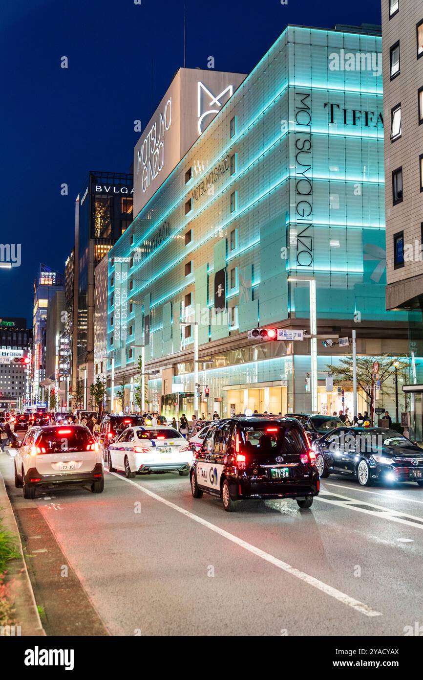 Die Ginza mit dem Wahrzeichen Matsuya Ginza und dem Tiffany Store Gebäude beleuchtet in blauem, grünem, diffusem Licht. Im Vordergrund, Verkehr an der Ampel. Stockfoto