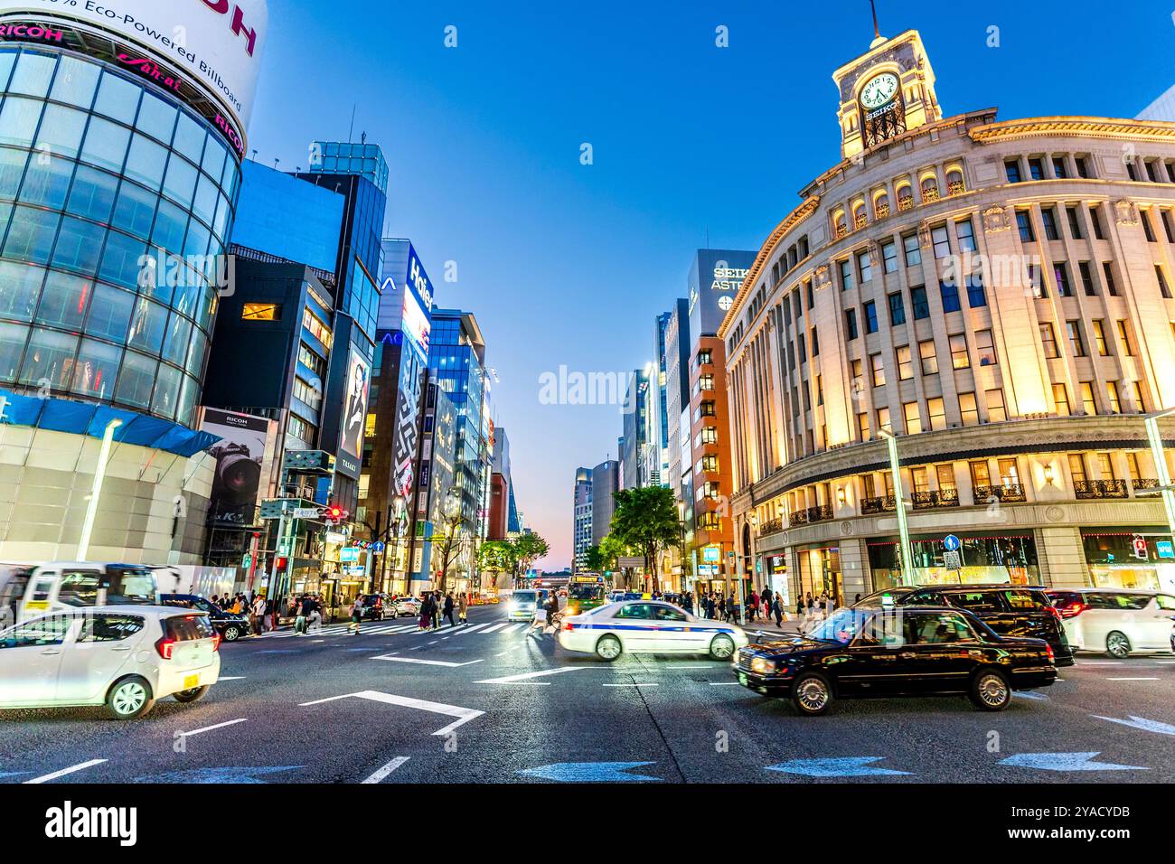 Blick entlang der Straße, Taxis fahren an der geschäftigen Kreuzung Ginza 4 vor dem Seiko House Gebäude (ehemals Wako Gebäude) während der abendlichen blauen Stunde Stockfoto