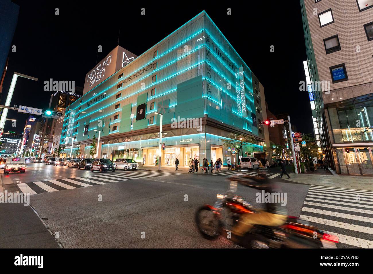 Ginza und das Geschäftsgebäude von Matsuya Ginza und Tiffany werden in blauem grünem Licht beleuchtet. Der Verkehr hielt an der Fußgängerüberquerung an, Radfahrer fuhren vorbei. Stockfoto