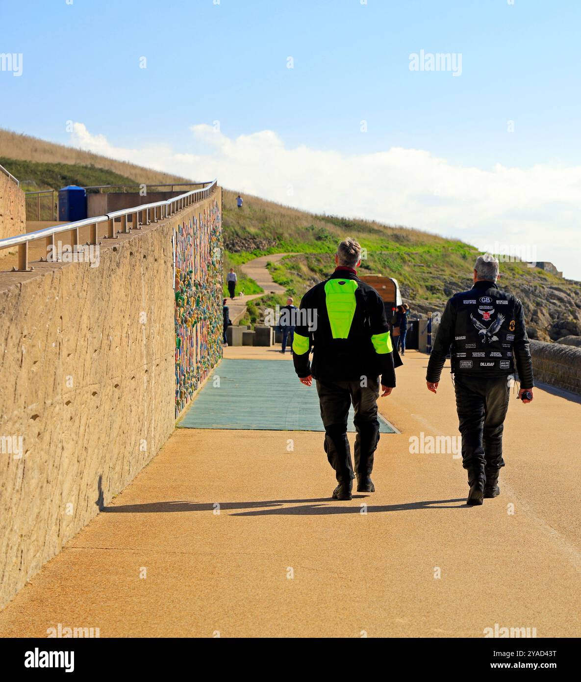 Zwei Männer gehen auf der Promenade auf Barry Island, Südwales, Großbritannien. Vom Oktober 2024. Amüsante Bikerjacke Stockfoto