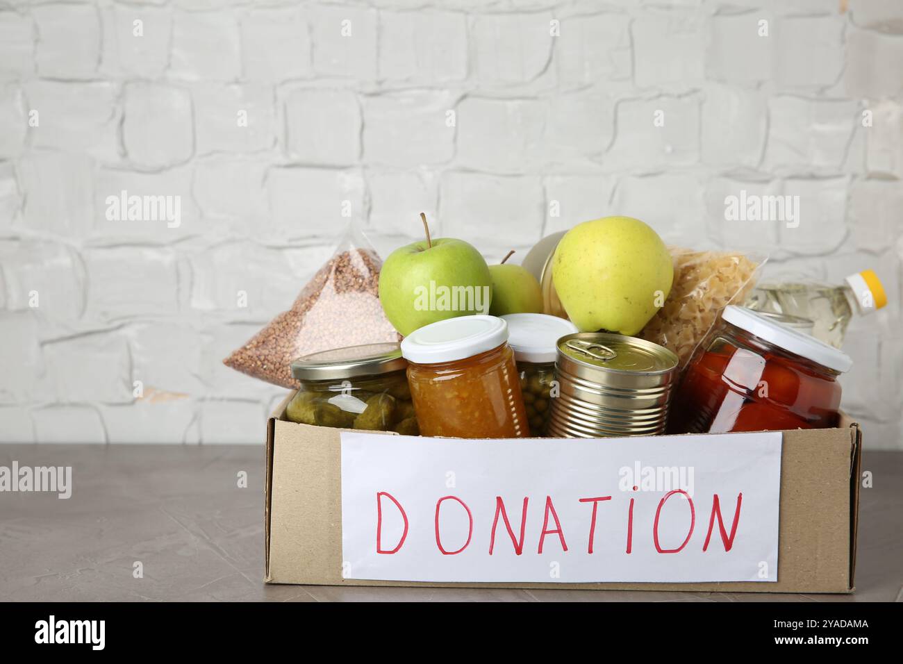 Verschiedene Produkte in Karton auf grauem Tisch. Lebensmittelspende Stockfoto