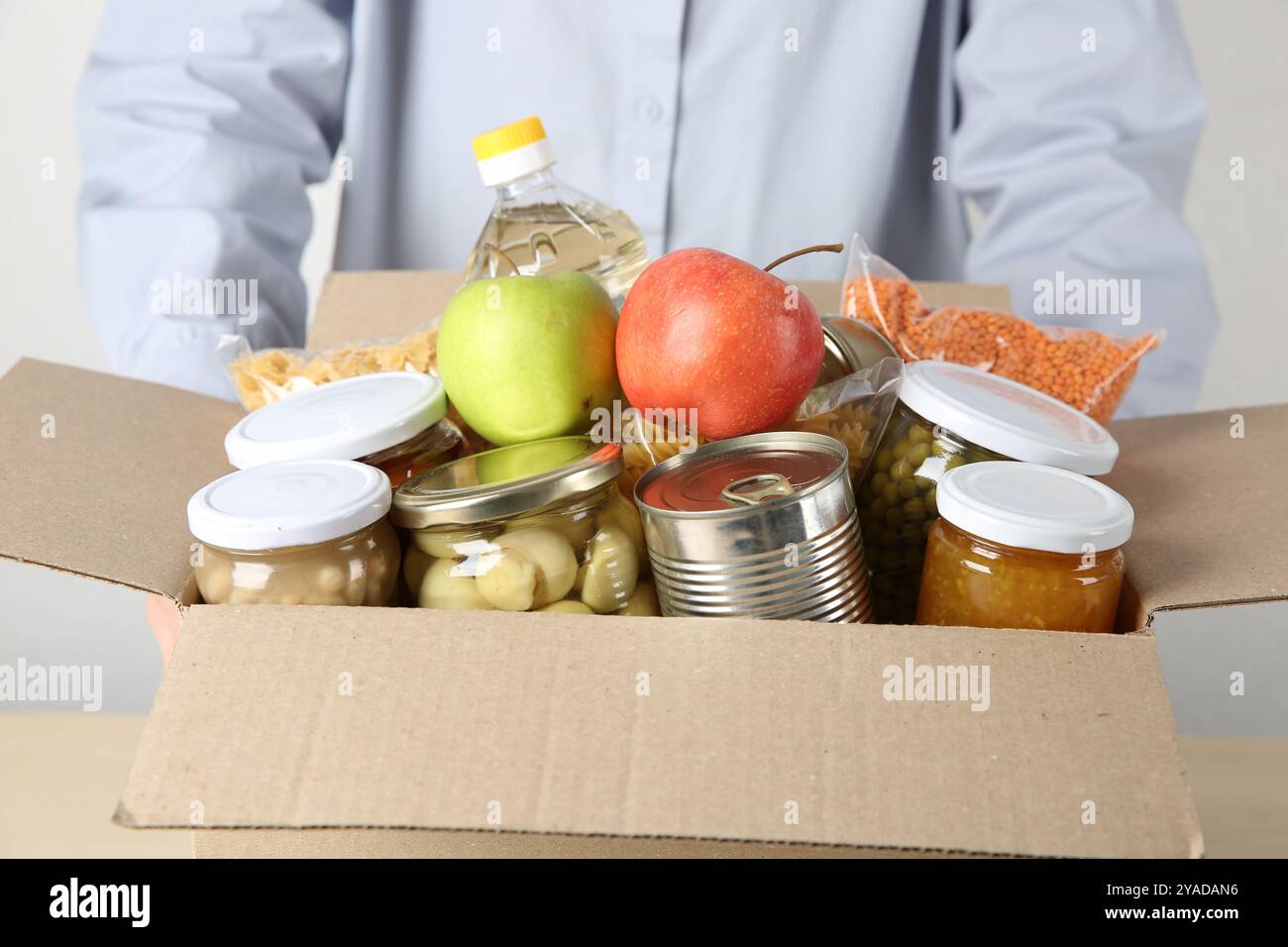 Lebensmittelspende. Frau mit Kiste verschiedener Produkte an Tisch drinnen, Nahaufnahme Stockfoto