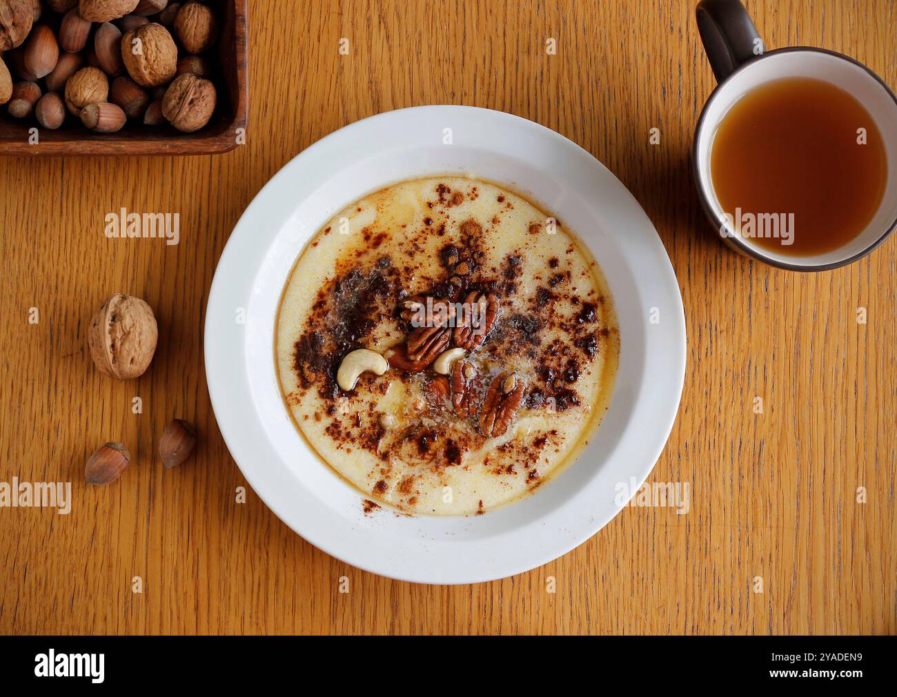 Gesunder glutenfreier Brei aus Buchweizen und Maisgrieß gekocht und auf weißem Teller mit Zimt, Ahornsirup, Butter und Nüssen serviert. Stockfoto