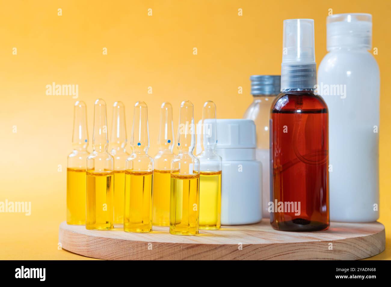 Eine Hand, die eine Ampulle hält, gefüllt mit gelber Flüssigkeit, umgeben von verschiedenen Flaschen mit Hautpflegeprodukten in verschiedenen Formen und Größen. Der Hintergrund Stockfoto