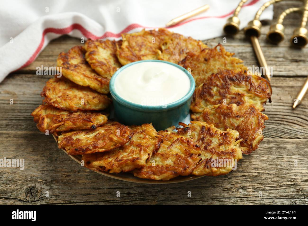 Leckere Kartoffelpfannkuchen, Sauerrahm, Menora und Kerzen auf Holztisch, Nahaufnahme. Hanukkah festliches Essen Stockfoto