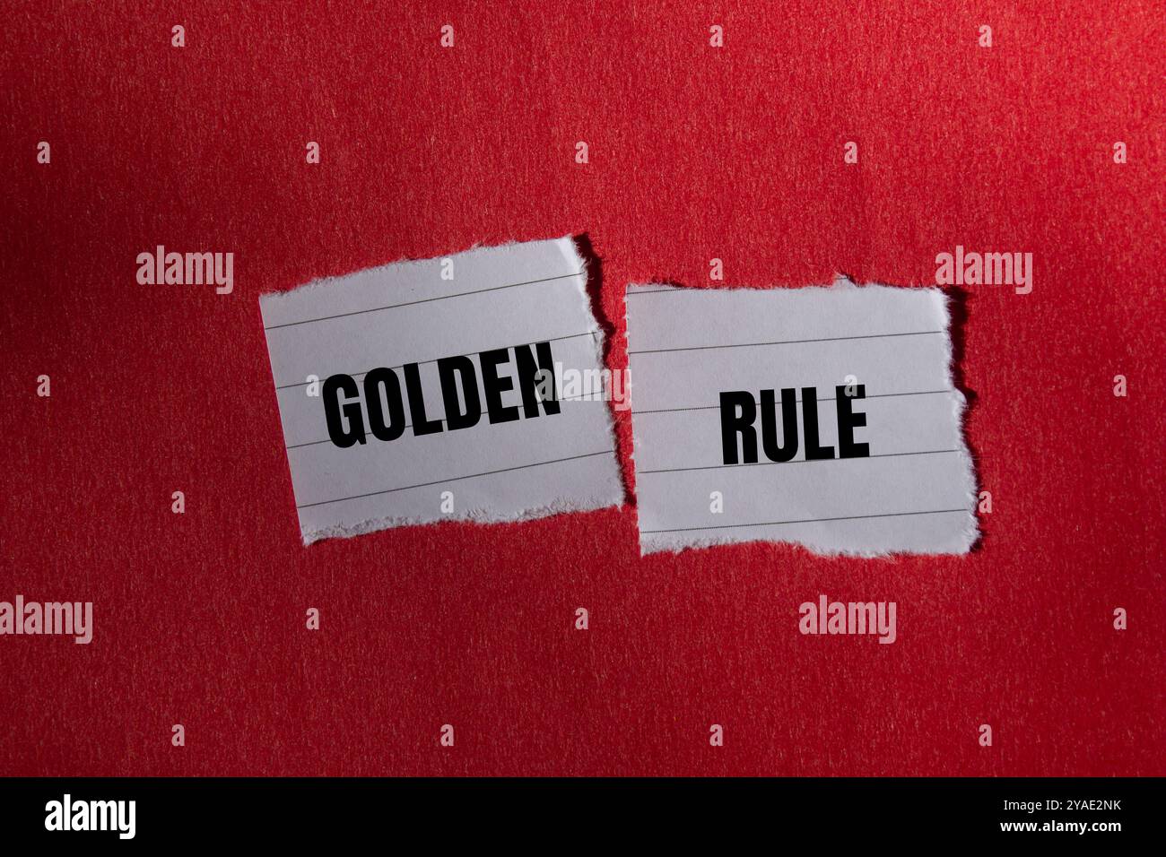 Goldene Regelnachricht auf gerissenem Papierstück mit rotem Hintergrund. Konzeptionelles goldenes Regelsymbol. Kopierbereich. Stockfoto