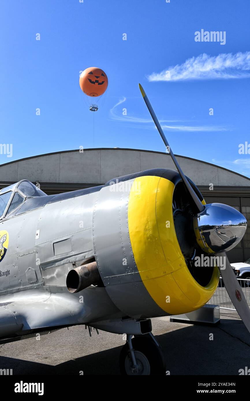 IRVINE, KALIFORNIEN - 11. OCT 2024: Antikes Flugzeug im Great Park mit Ballonfahrt mit Kürbisgesicht, das über dem Hangar ragt. Stockfoto