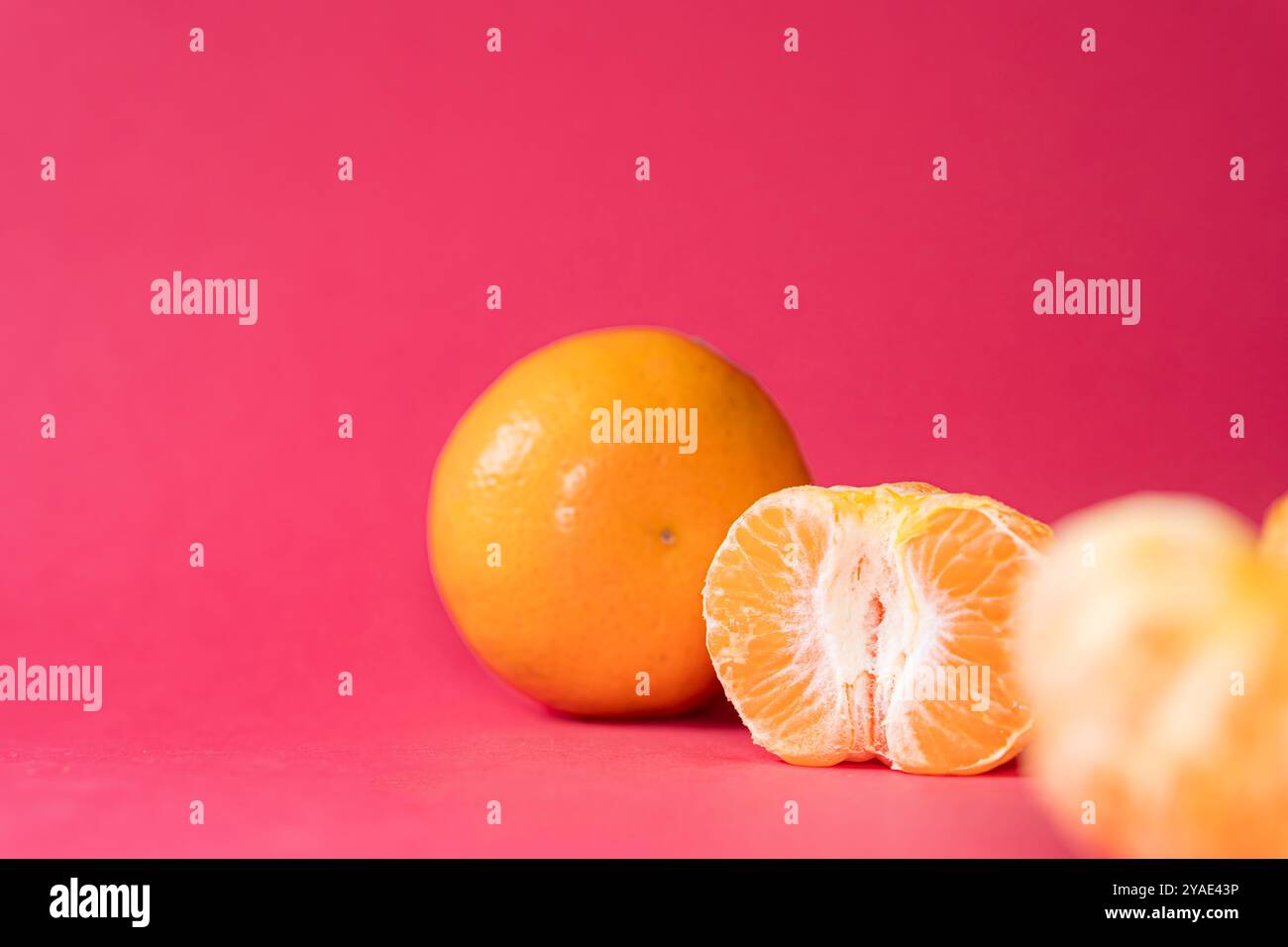 Zwei Orangen auf einem leuchtend rosa Hintergrund, eine Orange ist teilweise geschält und zeigt sein saftiges Interieur. Die hellen Farben sorgen für einen auffälligen Kontrast, Stockfoto