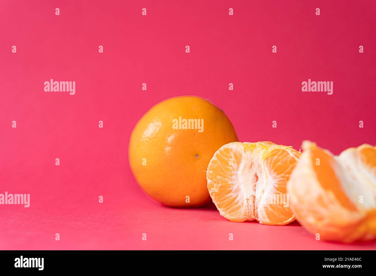 Zwei Orangen auf einem leuchtend rosa Hintergrund, eine Orange ist teilweise geschält und zeigt sein saftiges Interieur. Die hellen Farben sorgen für einen auffälligen Kontrast, Stockfoto