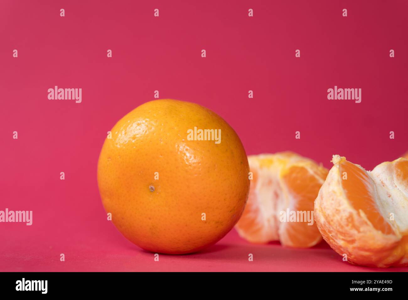 Zwei Orangen auf einem leuchtend rosa Hintergrund, eine Orange ist teilweise geschält und zeigt sein saftiges Interieur. Die hellen Farben sorgen für einen auffälligen Kontrast, Stockfoto