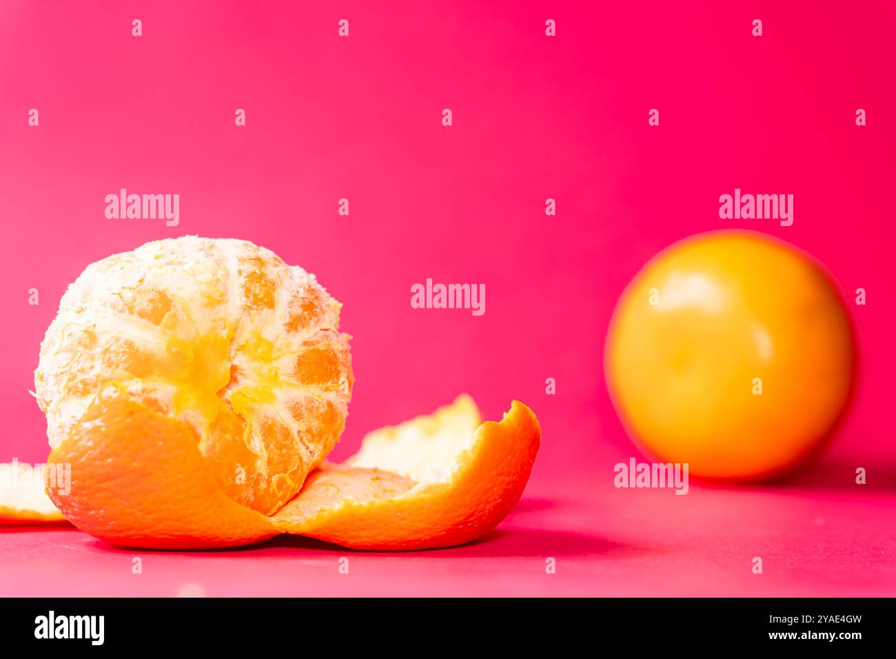 Zwei Orangen auf einem leuchtend rosa Hintergrund, eine Orange ist teilweise geschält und zeigt sein saftiges Interieur. Die hellen Farben sorgen für einen auffälligen Kontrast, Stockfoto