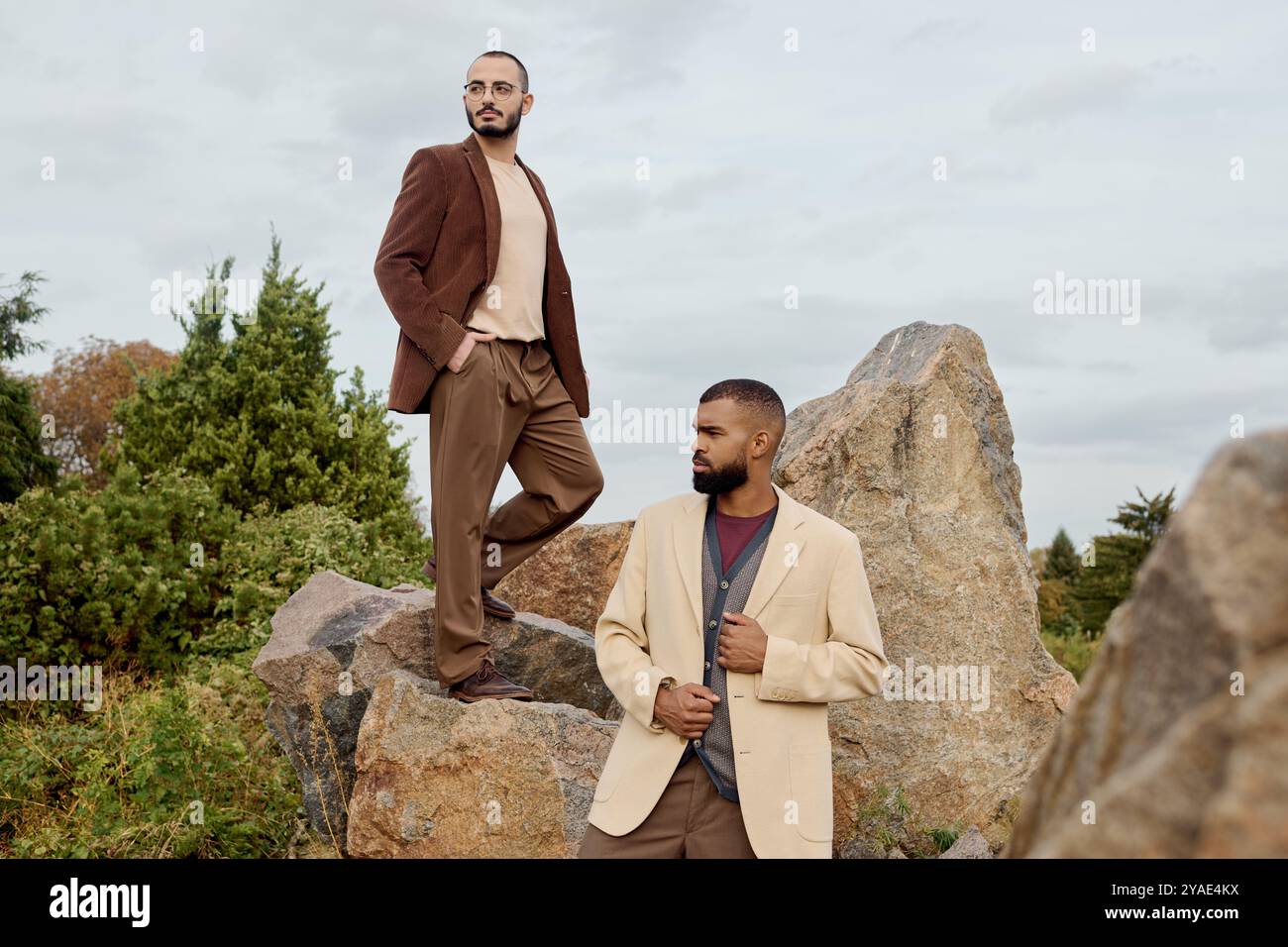 Hübsche Männer posieren selbstbewusst in stilvollen Herbstoutfits vor einer lebendigen natürlichen Kulisse. Stockfoto