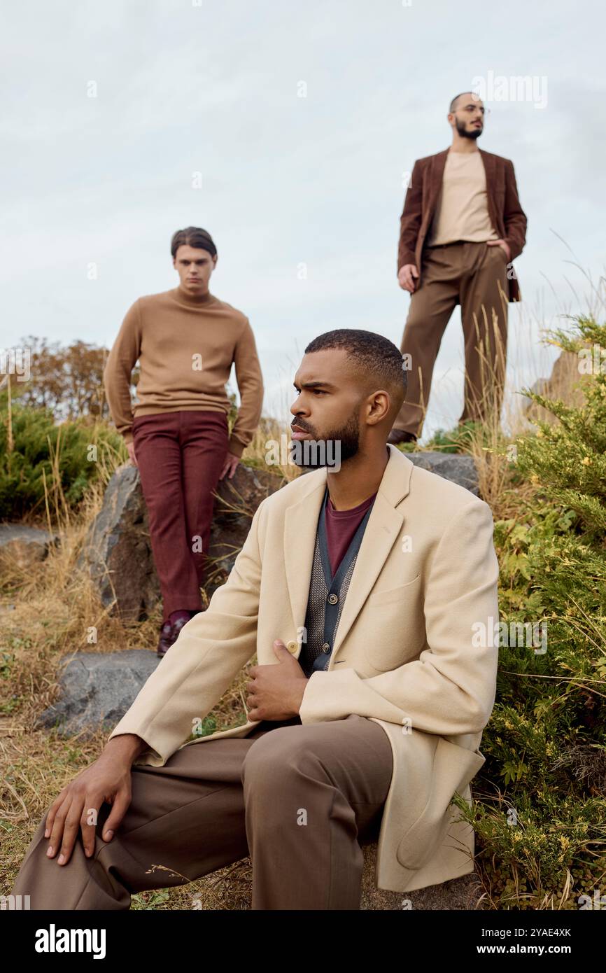 Drei gutaussehende Männer in modischen Herbstoutfits posieren nachdenklich in einer wunderschönen Naturlandschaft. Stockfoto