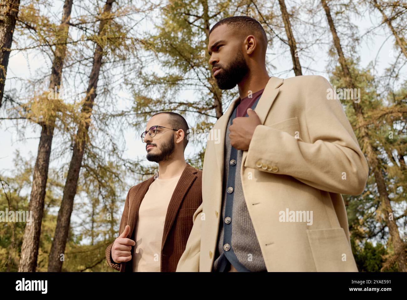 Zwei gut gekleidete Männer schlendern durch eine lebhafte Herbstlandschaft und genießen den Charme der Saison. Stockfoto