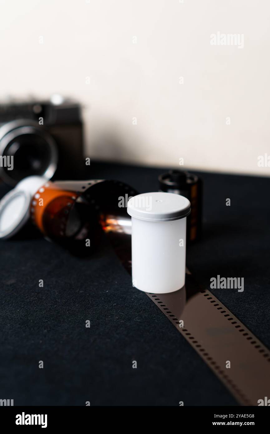 Eine Vintage-Kamera mit einer Rolle Film und einem weißen Filmkanister auf einer dunklen Oberfläche. Die Kamera ist im Hintergrund leicht unscharf, während die Fil Stockfoto