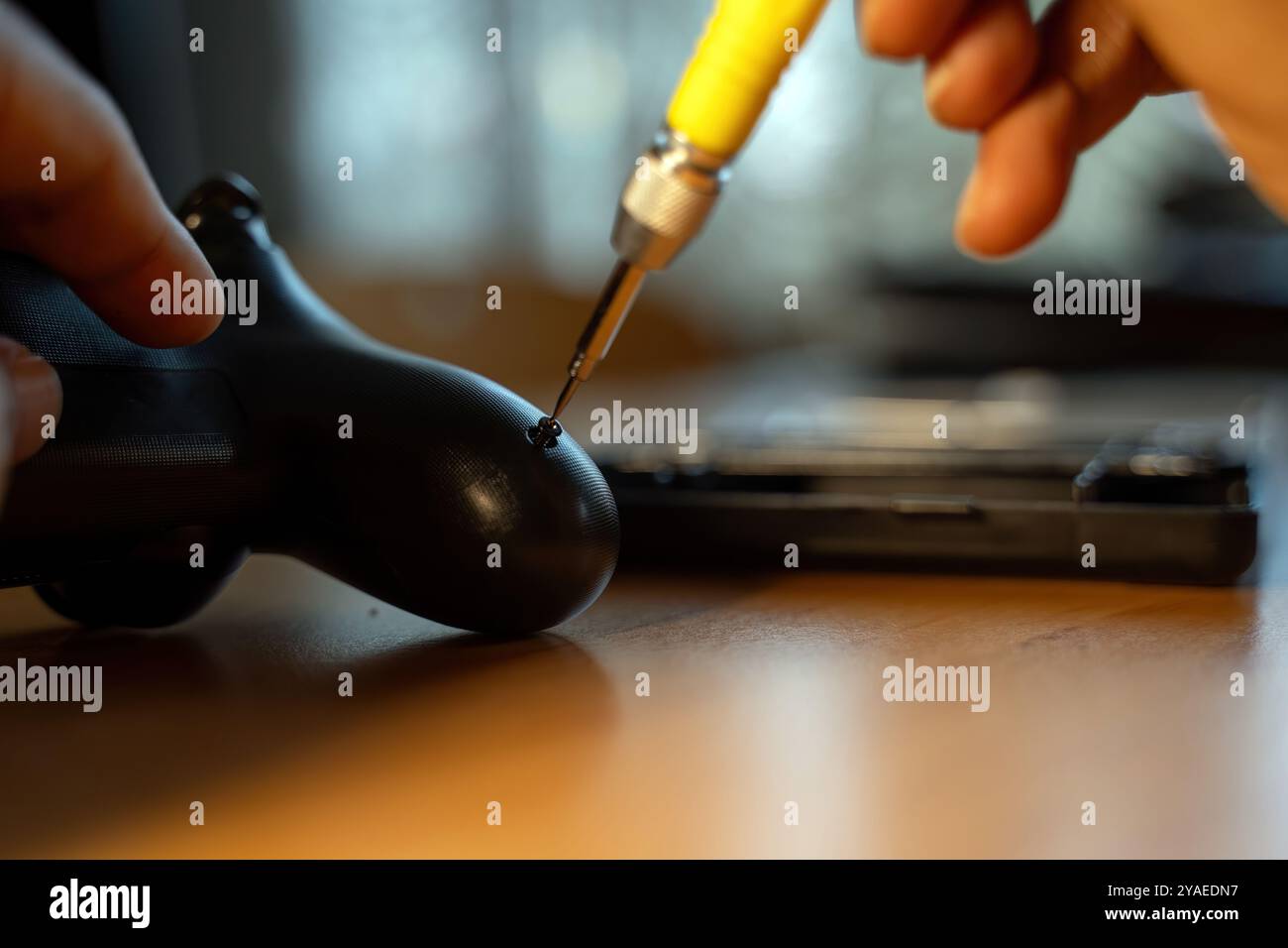 Eine detaillierte Nahaufnahme einer Hand mit einem Schraubendreher, um einen Videospiel-Controller zu reparieren, wobei Präzision und technische Fähigkeiten hervorgehoben werden. Das Bild zeigt die Stockfoto