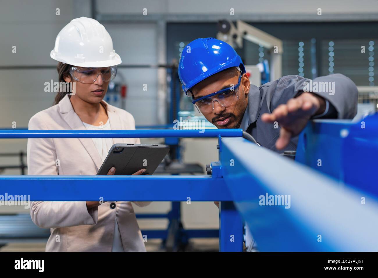 Afroamerikaner Ingenieur und eine Inderin, eine Fabrikleiterin, die ein Tablet hält, durch die Produktionslinie läuft, Inspektionen durchführt, Vorderansicht. Stockfoto