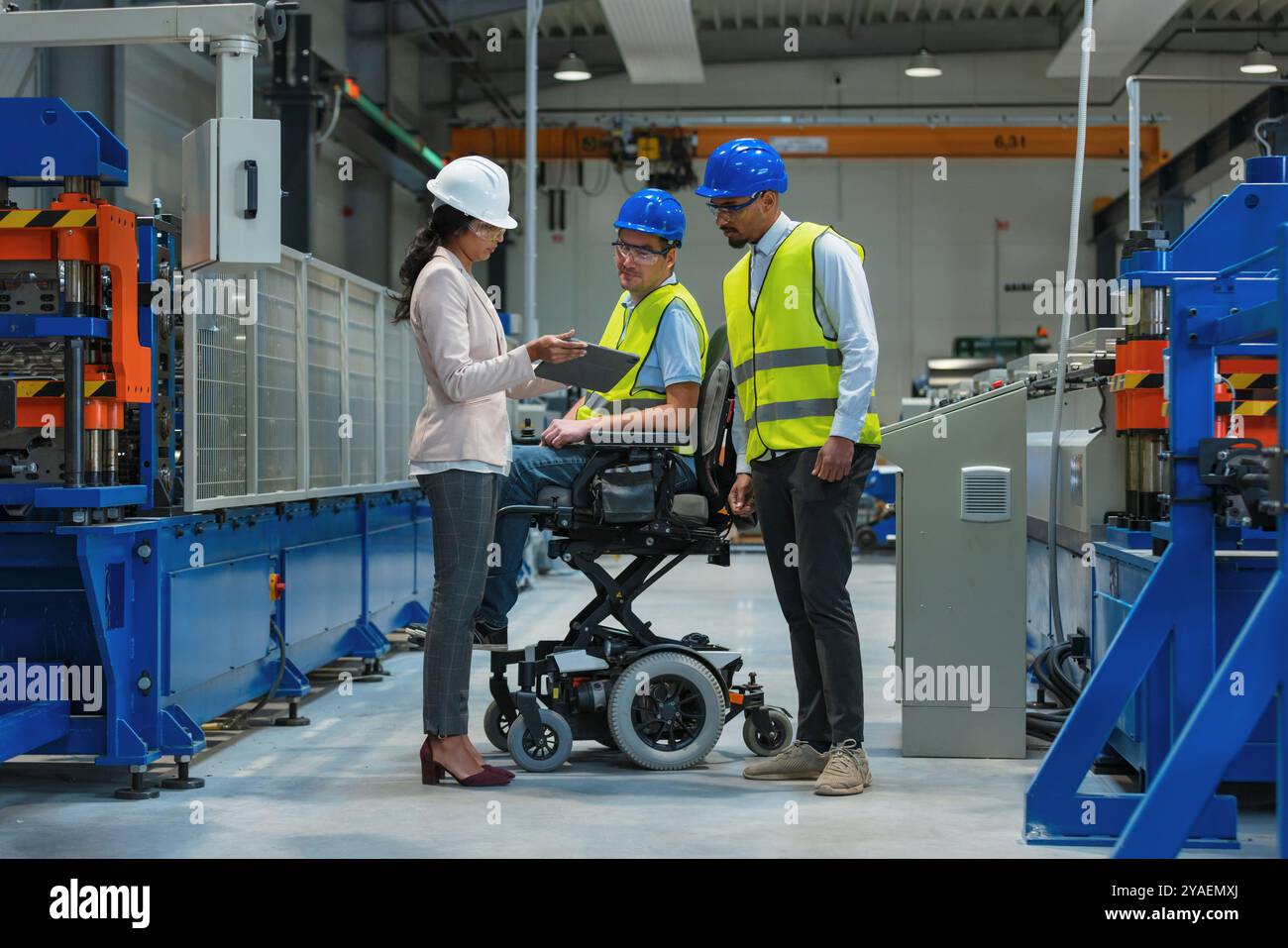 Weibliche Führungskraft spricht mit zwei Arbeitern an der Produktionslinie, darunter einer mit Behinderung, über den Produktionsprozess. Stockfoto