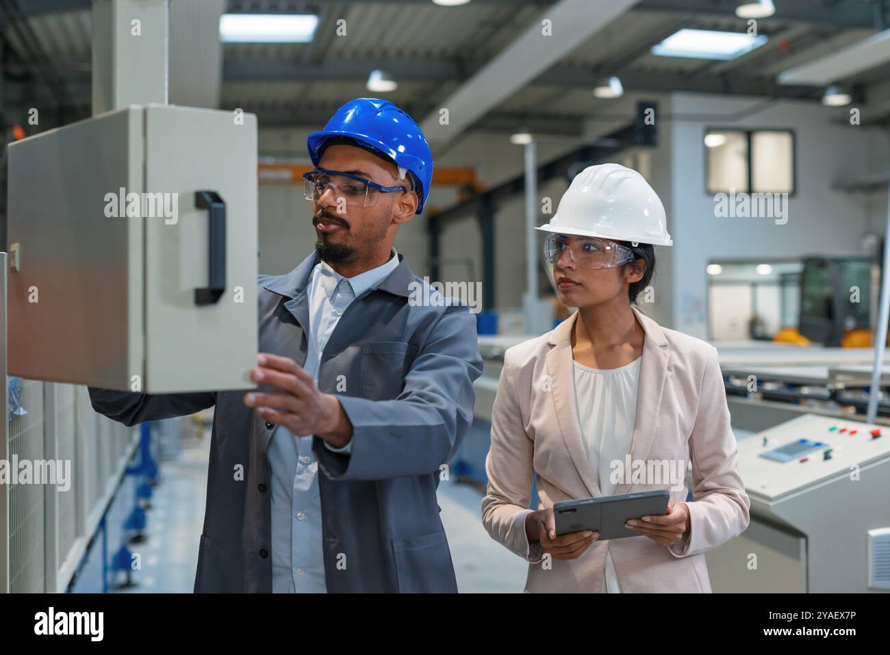 Indische Managerin und afroamerikanischer Chefingenieur gehen durch die Fabrik, sprechen und planen Produktionsoptimierung, Vorderansicht. Stockfoto