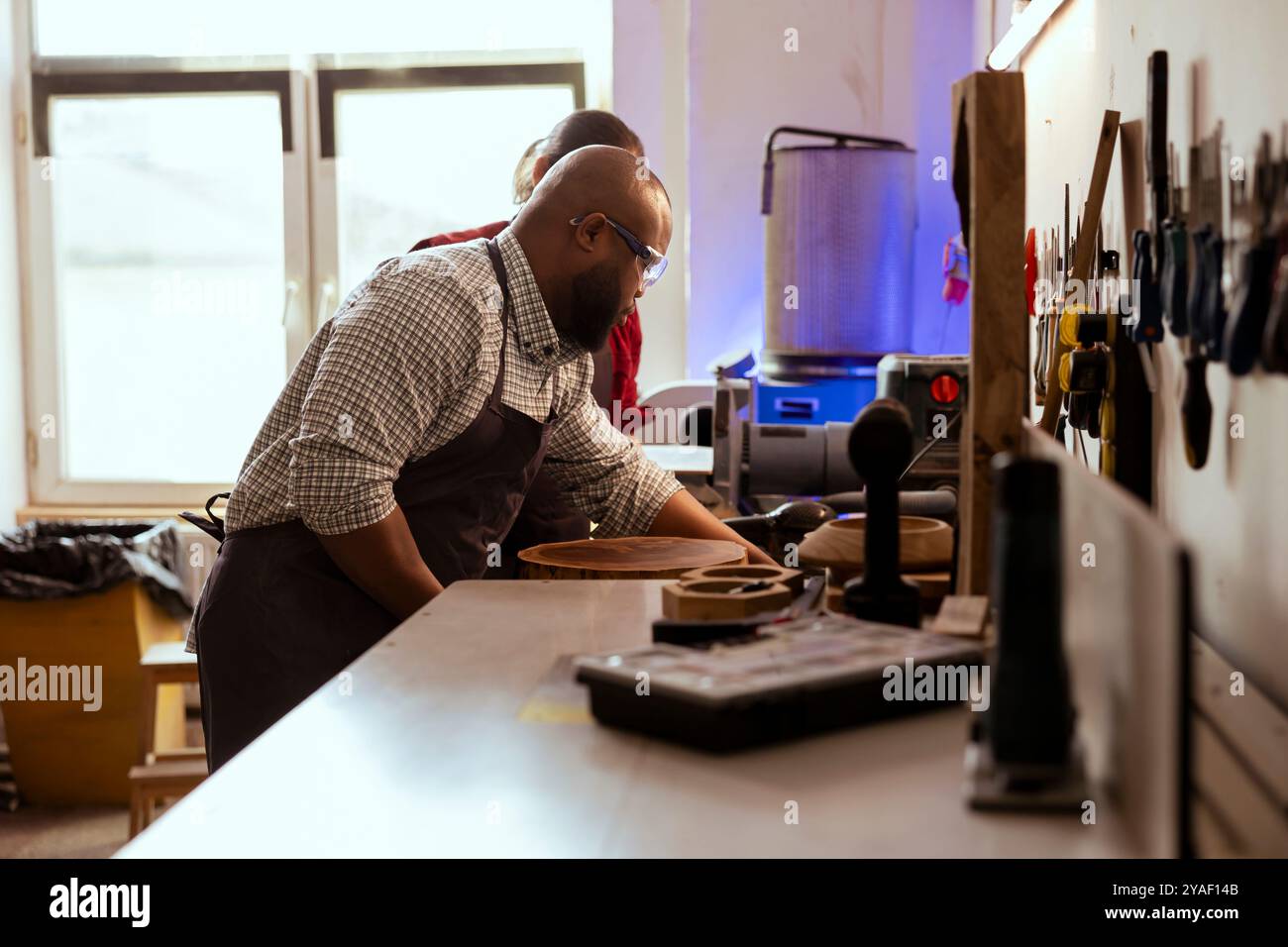 afroamerikanischer Zimmermann, der Holzmaterialien sammelt, unterstützt von einem Kollegen. BIPOC Tischler und Kollege, der Qualitätssicherung für Holzblöcke durchführt und sicherstellt, dass es für die Möbelmontage verwendet werden kann Stockfoto