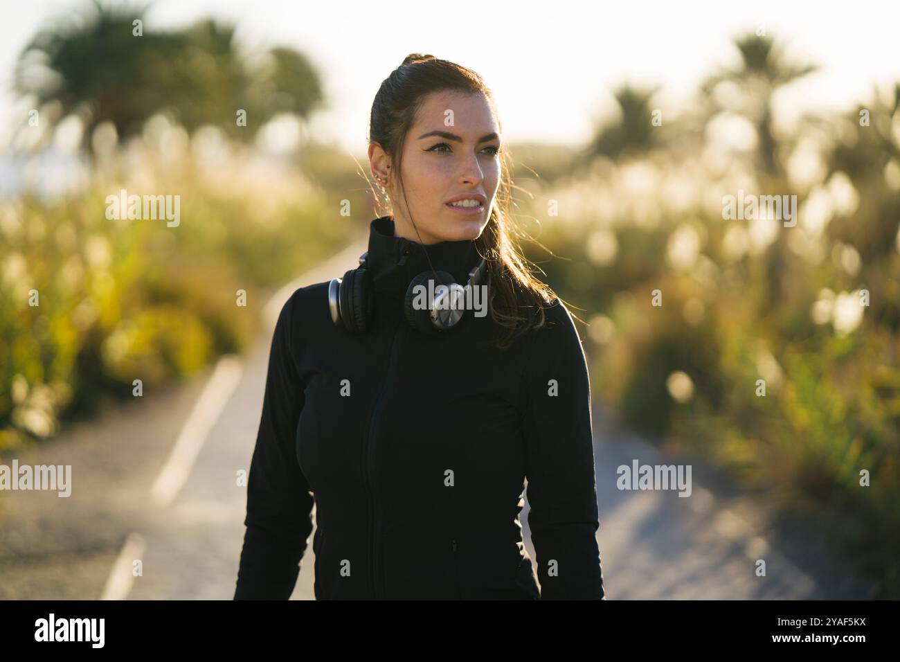 Junge Frau in lebendiger Activewear genießt die Natur und hört Musik mit Kopfhörern Stockfoto