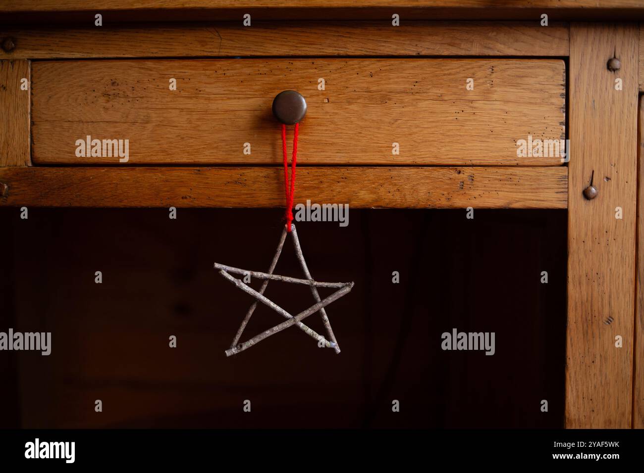 Handgefertigtes Sternenschmuck aus Zweigen, die an Holztür hängen, mit roter Schnur. Rustikale Weihnachtsdekoration in heimischem Ambiente. Winterurlaub und festliche Deko Stockfoto