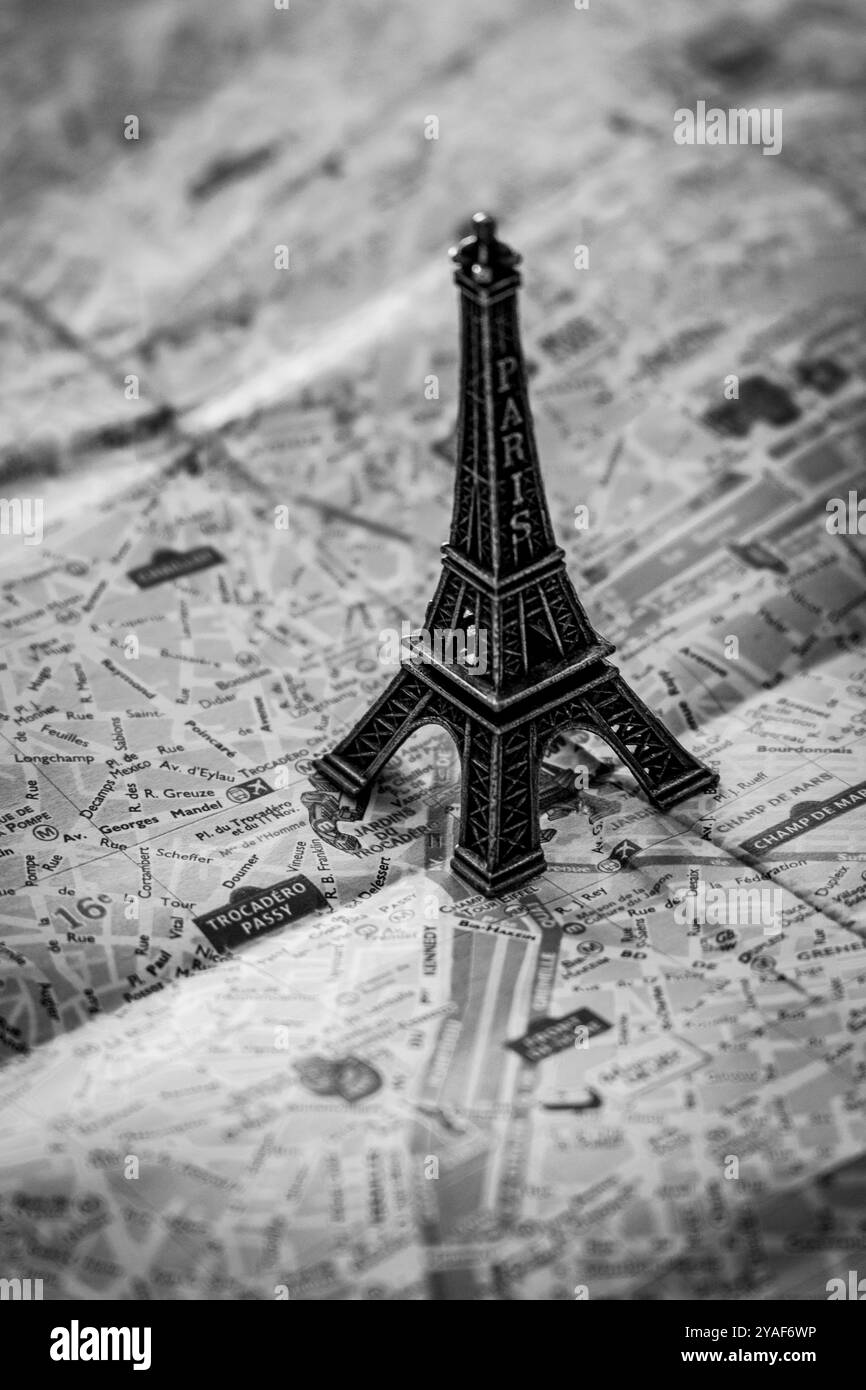 Eine Miniatur-Replik des Eiffelturms aus Metall ragt über der Straßenkarte von Paris zur Illustration und Unterhaltung in Schwarz-weiß Stockfoto