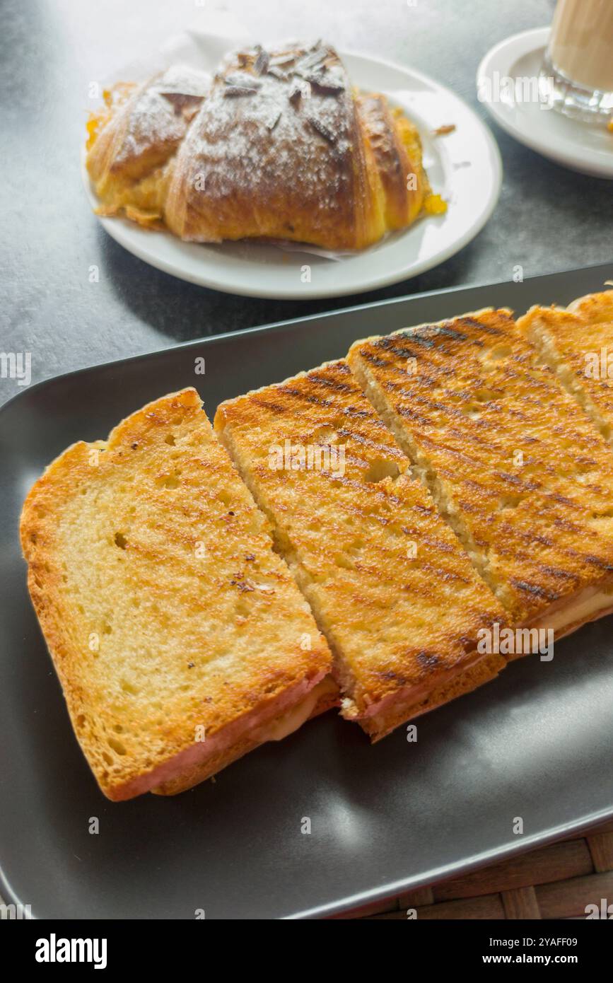 Geröstetes Schinken-Käse-Sandwich und süßes Brötchen auf dem Boden. Salzige und süße Kombination zum Frühstück Stockfoto