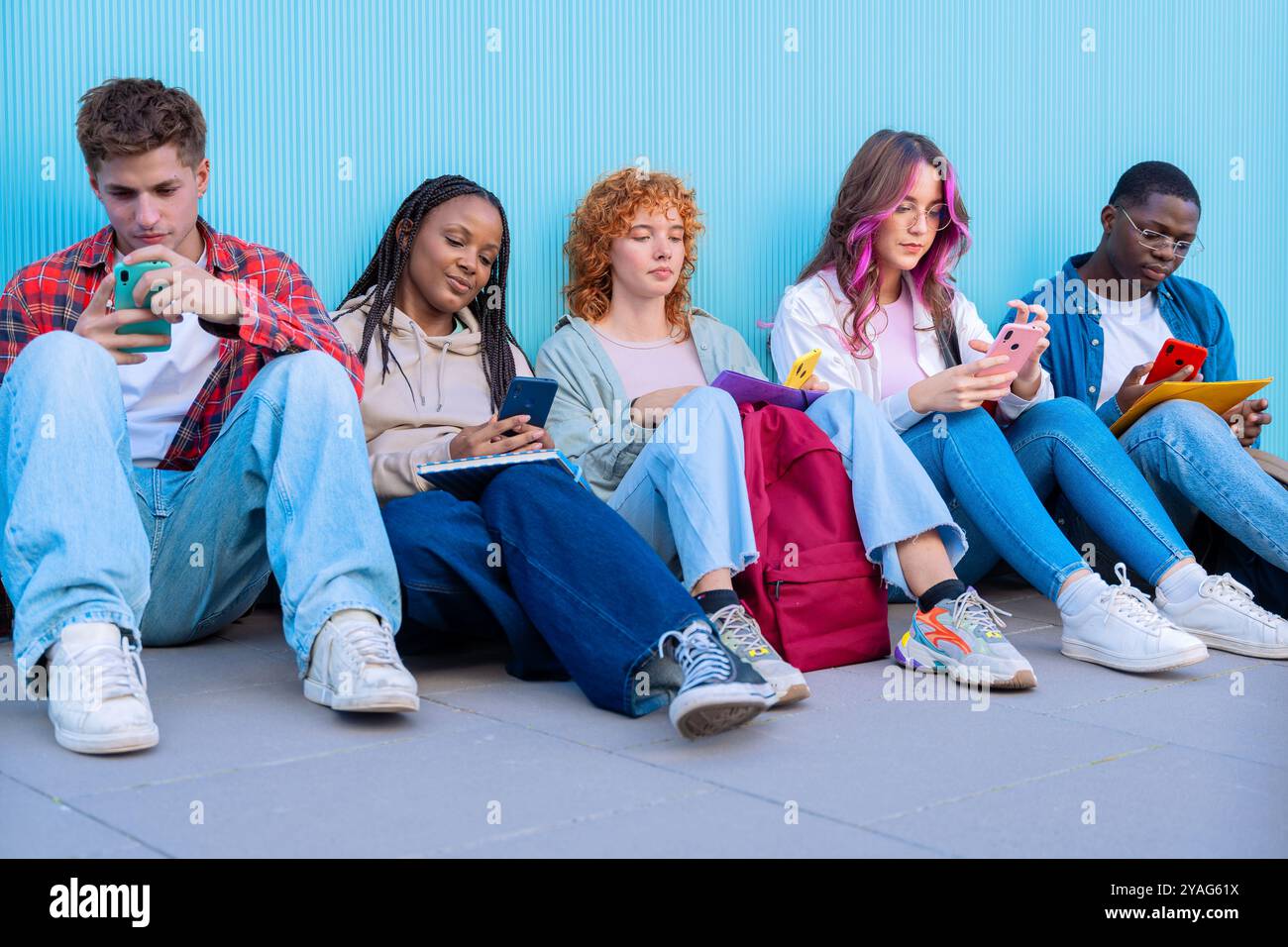 Eine Gruppe verschiedener junger Menschen, die im Freien mit Smartphones und Notebooks sitzen Stockfoto