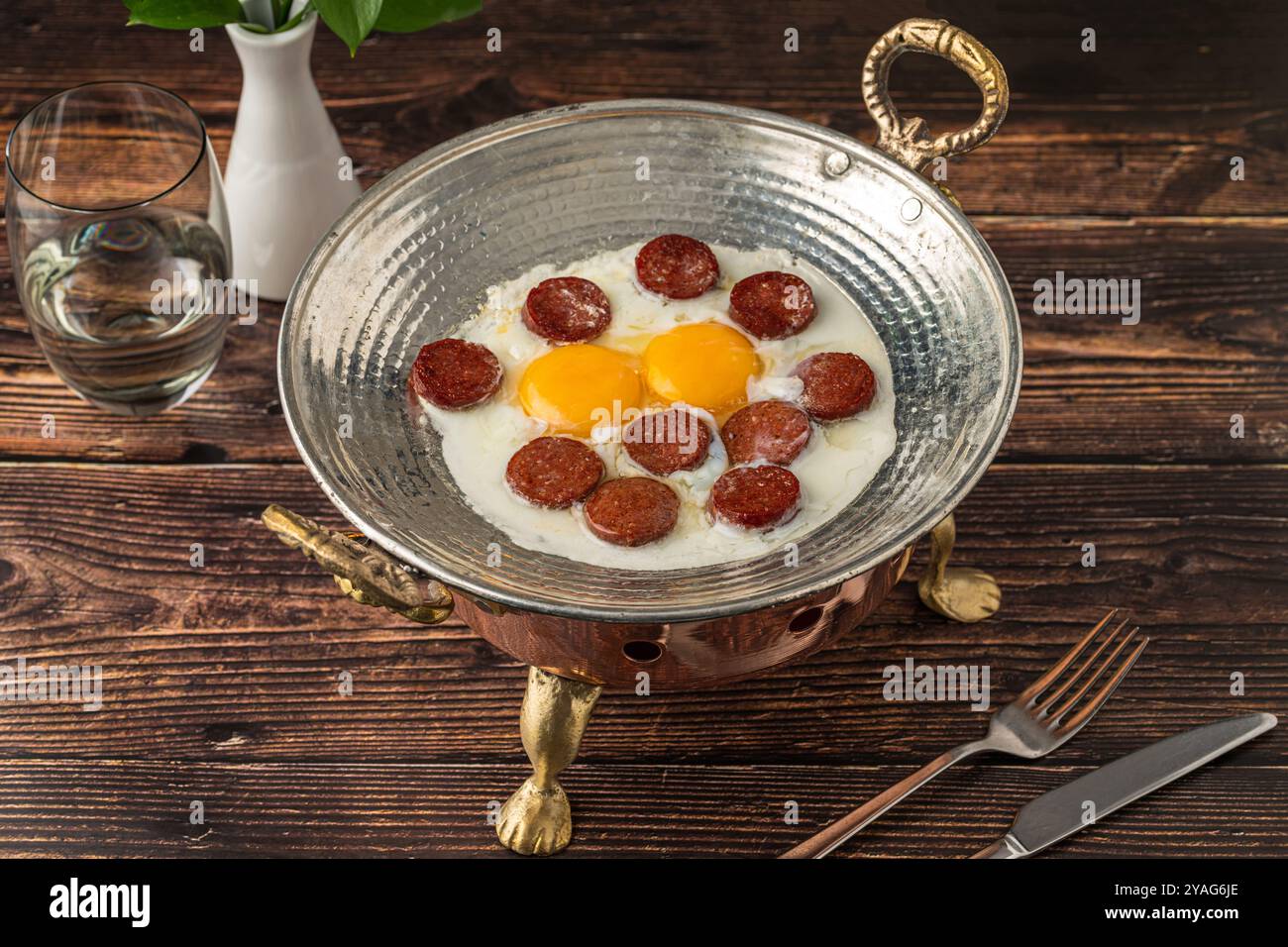 Eier mit türkischer Wurst in einer Kupferpfanne auf einem Holztisch. Türkischer Name sucuklu yumurta Stockfoto