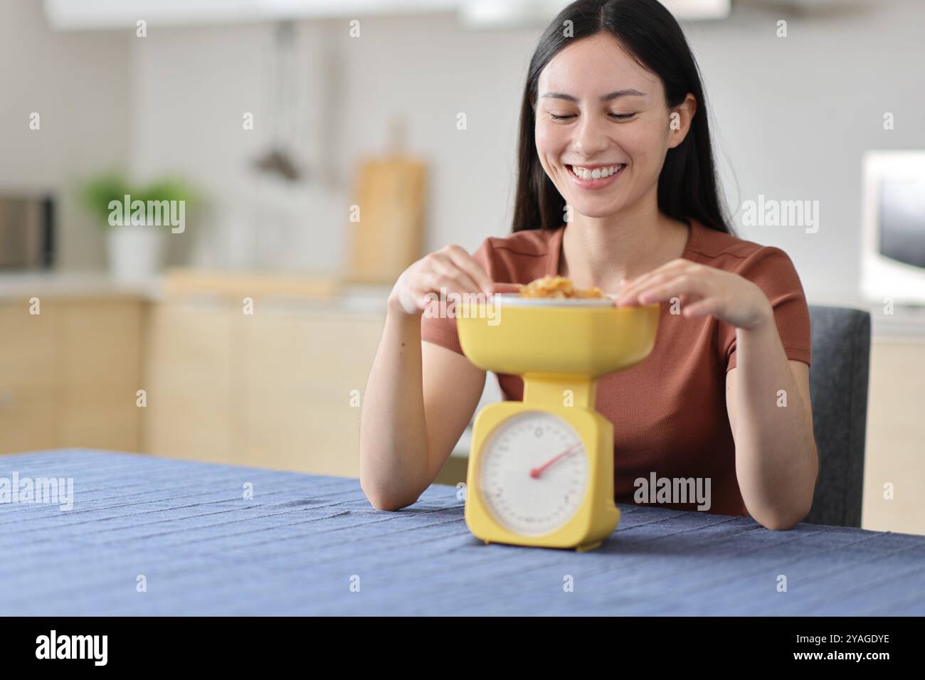 Glückliche asiatische Frau, die in der Küche zu Hause Essen mit Waage wägt Stockfoto