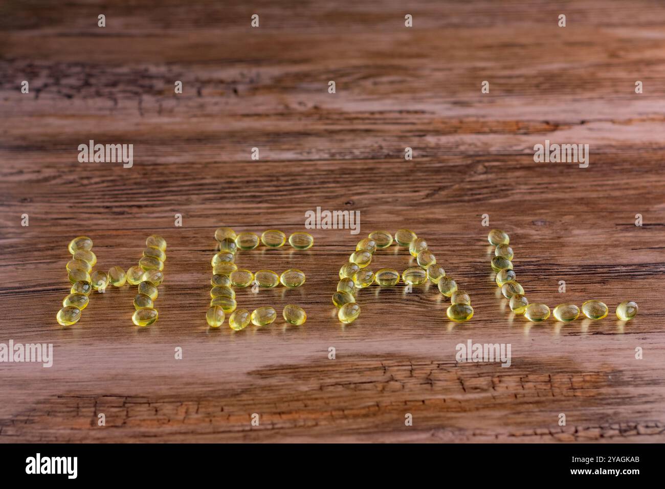 Eine hölzerne Oberfläche mit dem Wort "HEILEN", geschrieben mit gelben Pillen. Die Buchstaben bestehen aus kleinen, runden Objekten. Stockfoto