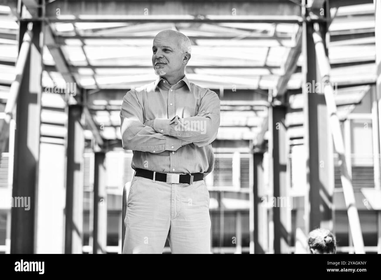 Der leitende Ingenieur steht vor einem Industriegebäude und sieht mit gekreuzten Armen selbstbewusst aus. Das Bild vermittelt Erfahrung und Fachwissen in Stockfoto