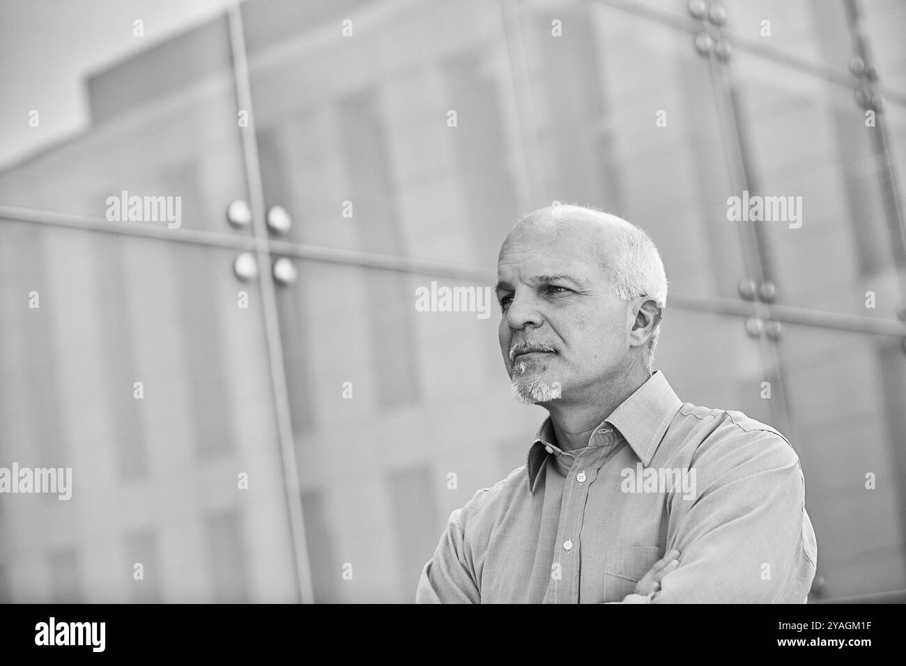 Schwarz-weiß-Porträt eines selbstbewussten Geschäftsmannes, der mit überkreuzten Armen vor einem modernen Bürogebäude steht Stockfoto