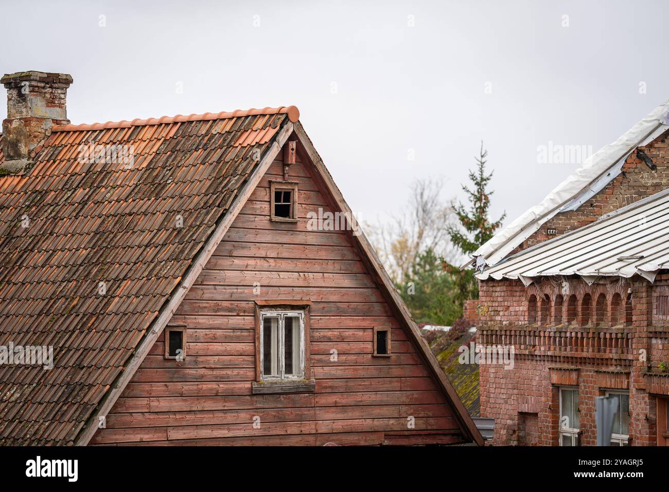 Zwei Häuser mit Anzeichen von Verfall, eine hölzerne Residenz und ein Backsteingebäude. Gebäude, die renoviert werden müssen. Stockfoto