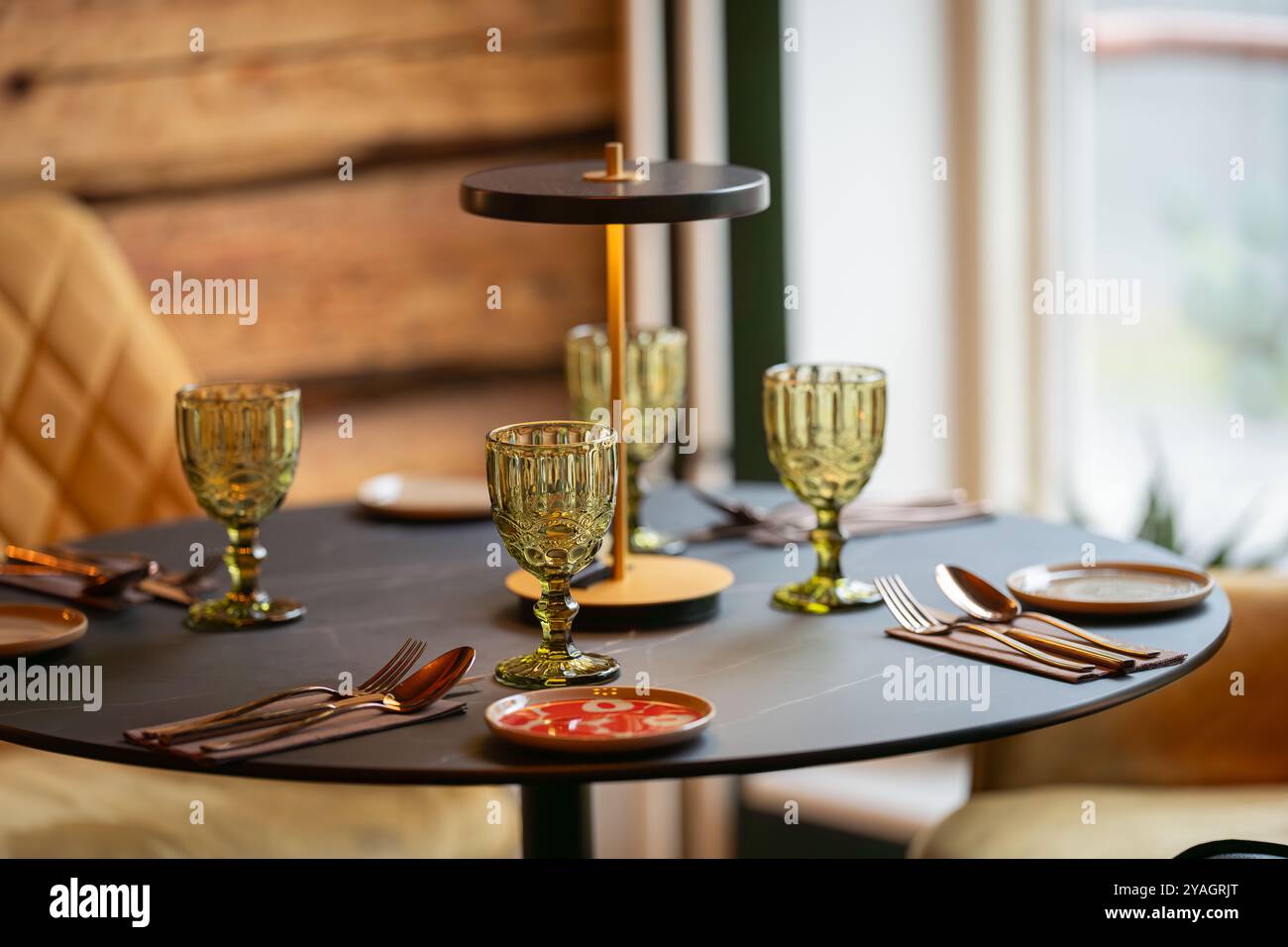 Ein runder, servierter Tisch steht für Gäste bereit. Runder Tisch mit leerem Teller, Gläsern, Gabeln, Serviette. Eleganter Esstisch. Stockfoto