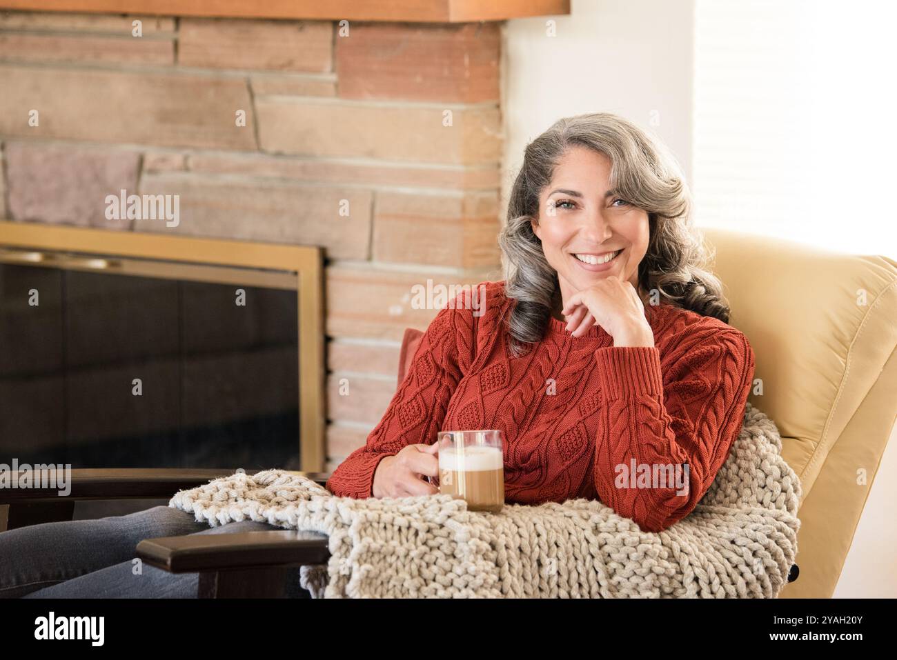 Gemütliche Frau, die zu Hause mit Kaffee lächelt Stockfoto